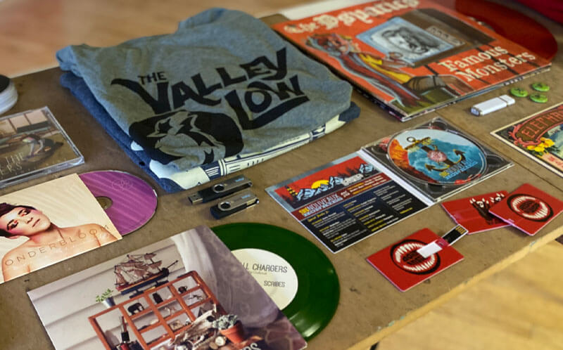 Band merchandise table with CDs, vinyl records, and t-shirts for sale